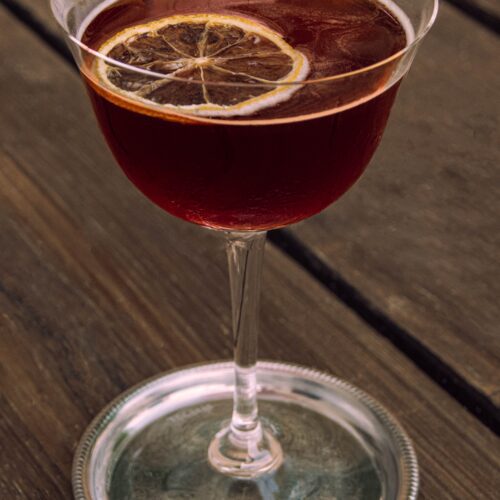 A wine glass of damson gin with a lemon slice garnish