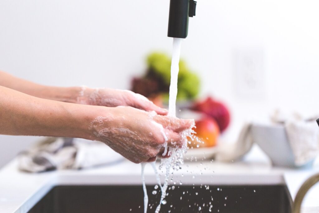 Hands being washed under running water at the kitchen sink