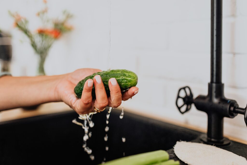 Hand washing a cucumber under running water at sink