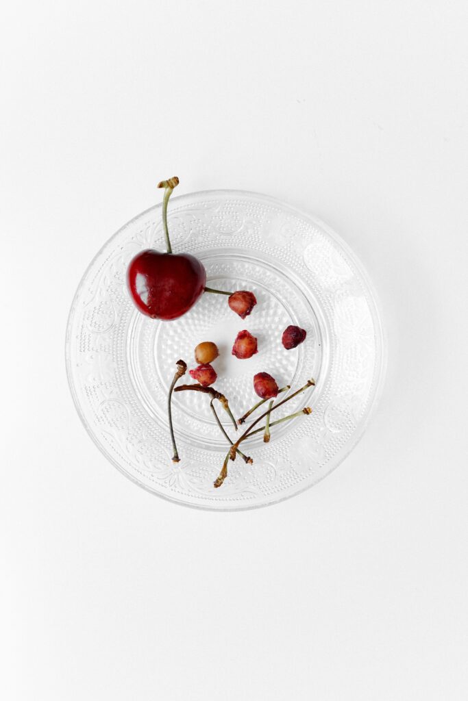 Plate with one whole cherry and a collection of cherry stalks and stones after using a cherry stone remover