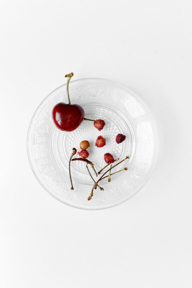 Plate with one whole cherry and a collection of cherry stalks and stones