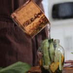 Person pouring brine into a jar of cucumber slices for pickling.