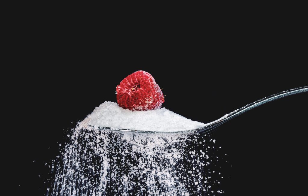 A single raspberry sat on a spoonful of white sugar