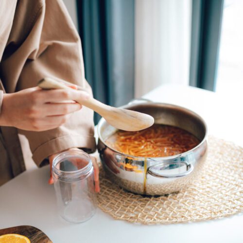 Person with wooden spoon preparing to ladle marmalade into a glass jar