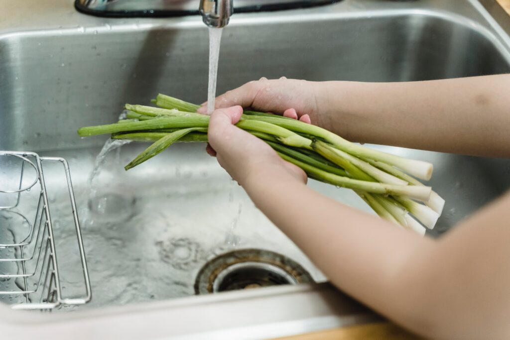 Person washing a bunch of spring onions under running water at sink