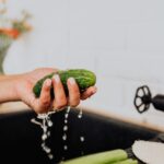 A person shaking excess water off a wahsed cucumber over the sink