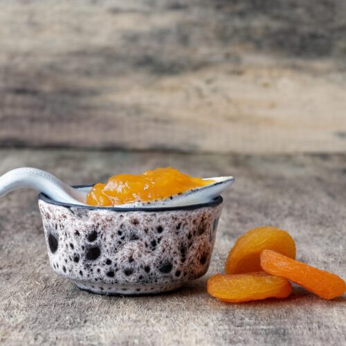 Ceramic jar with apricot jam with dried apricots on adjacent surface