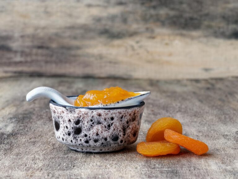 Ceramic jar with apricot jam with dried apricots on adjacent surface