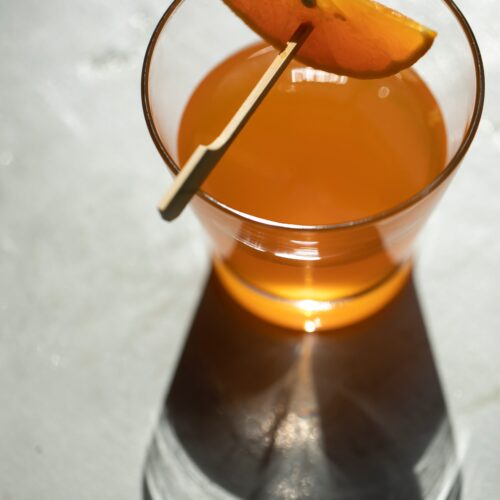 Orange liqueur in a glass, seen from above, with thin orange wedeg on a tooth-pick suspended over the glass