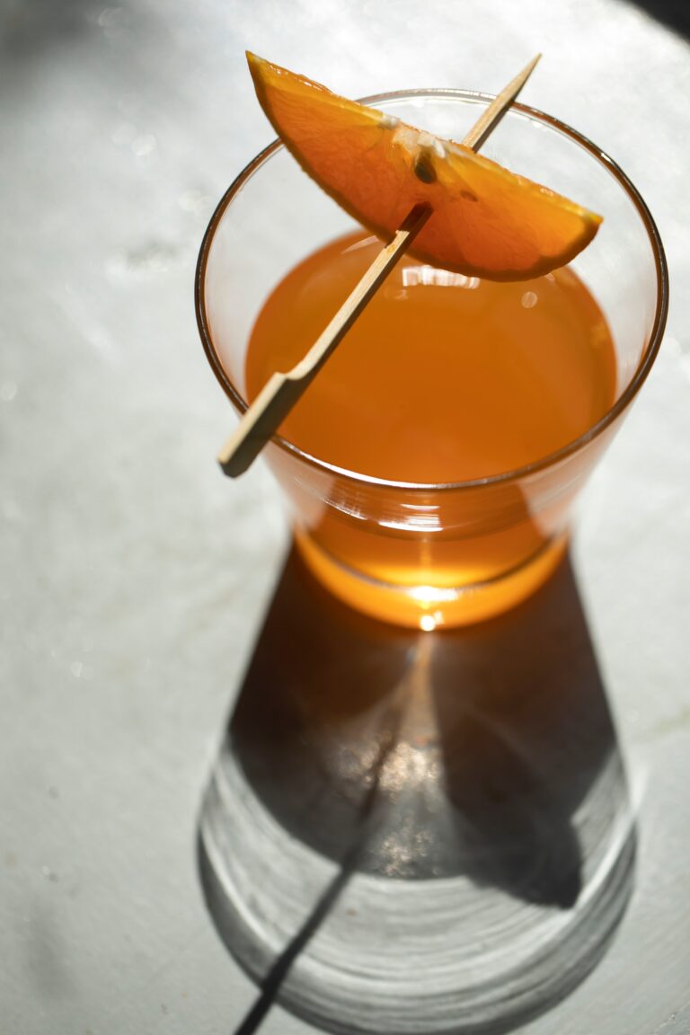 Orange liqueur in a glass, seen from above, with thin orange wedeg on a tooth-pick suspended over the glass