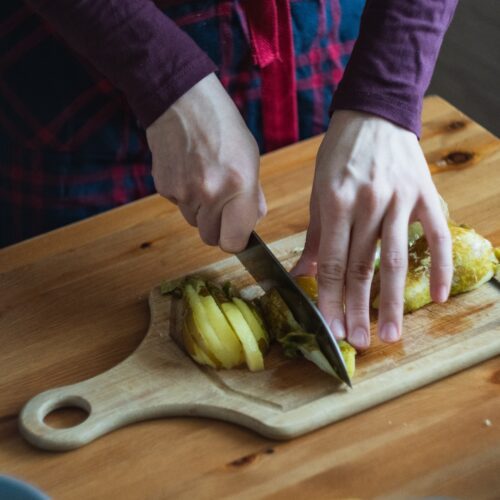 Persons hands chopping up pears on a wooden board, Another yellow handled knife, an egg in foreground on wooden work surface