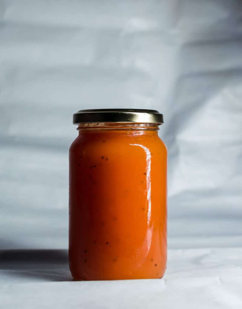 Jat of carrot jam with balck lid, standing on white surface