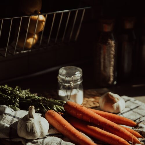 Bunch of carrots with garlic bulbs on chopping board with jar of salt nearby