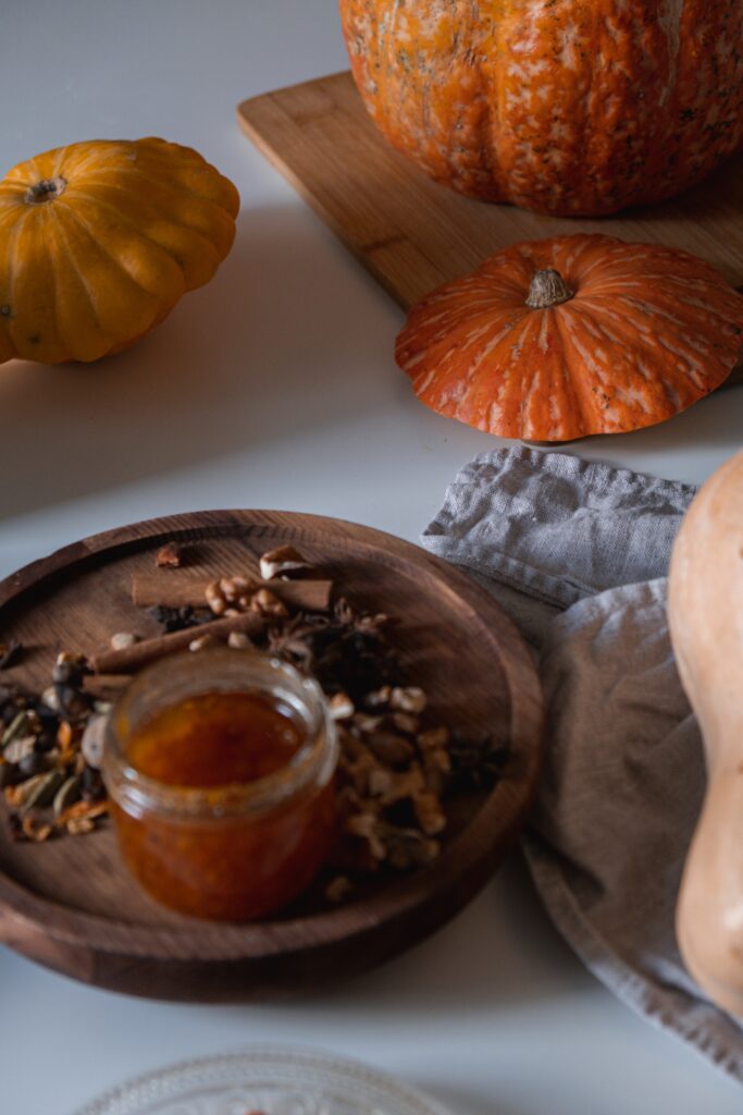 Pumpkins and squash on wooden board. In the forground a jar of pumkin and ginger jam on a smll wooden board surrounded by spices