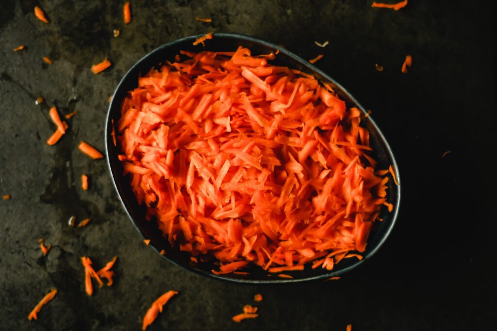 A dark bowl full of grated carrots on a dark stone background