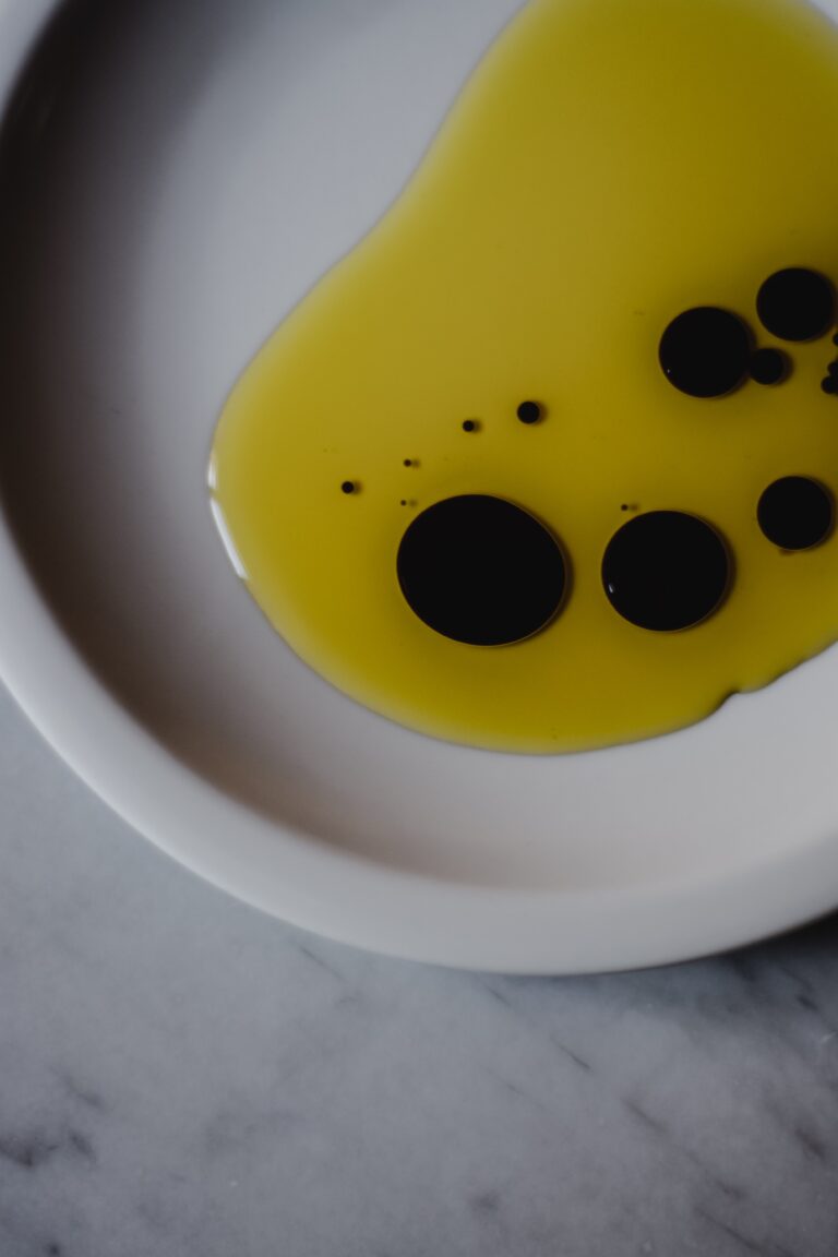 White bowl from above with pool of oil and dots of blackberry vinegar in it.