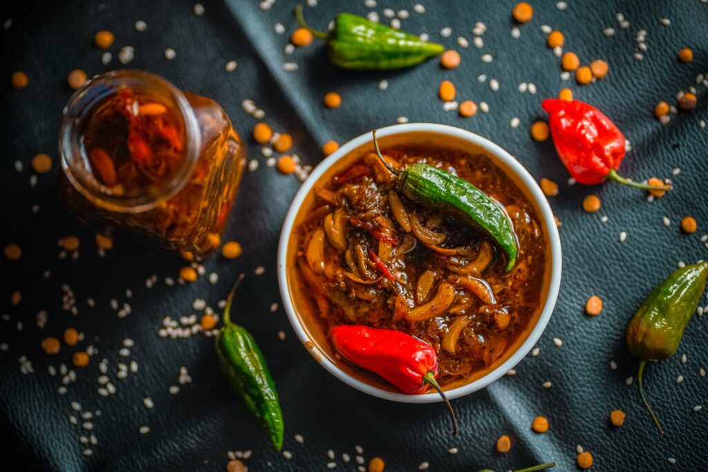 White bowl of carrot chutney with a red and green chilli garnish. A boolte of chutney and red and green peppers on the surface around the bowl.