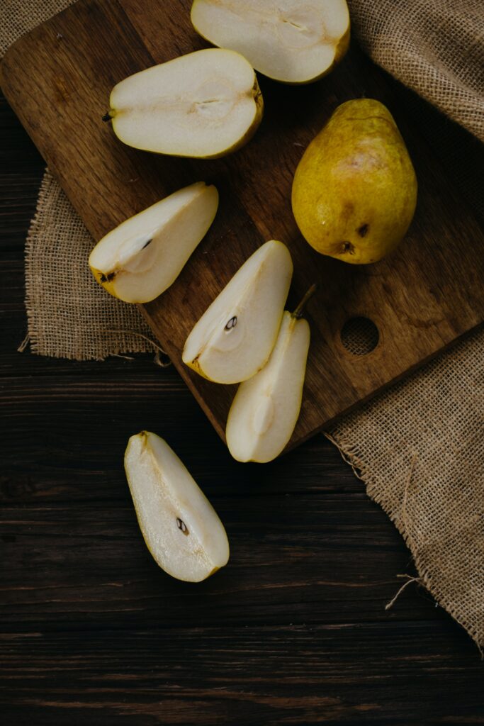 Whole pear, halved pears and quarters of pears on a wooden chopping board and a darker wooden work surface