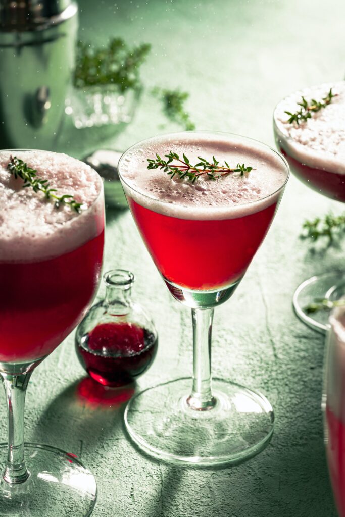 3 glasses of plum gin topped up with soda water and agrniched with a sprig of thyme. A small bottle of drak plum gin in the background