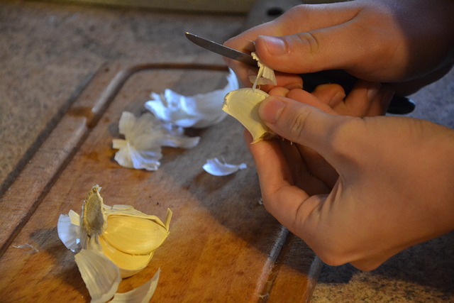 Persons hands peeling garlic with knife.