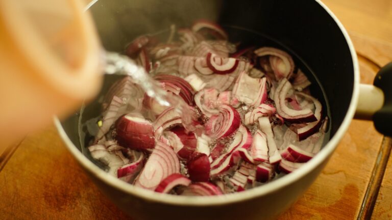 Ingredients in a stainless steel preserving pan with clear liquid being poured into it.