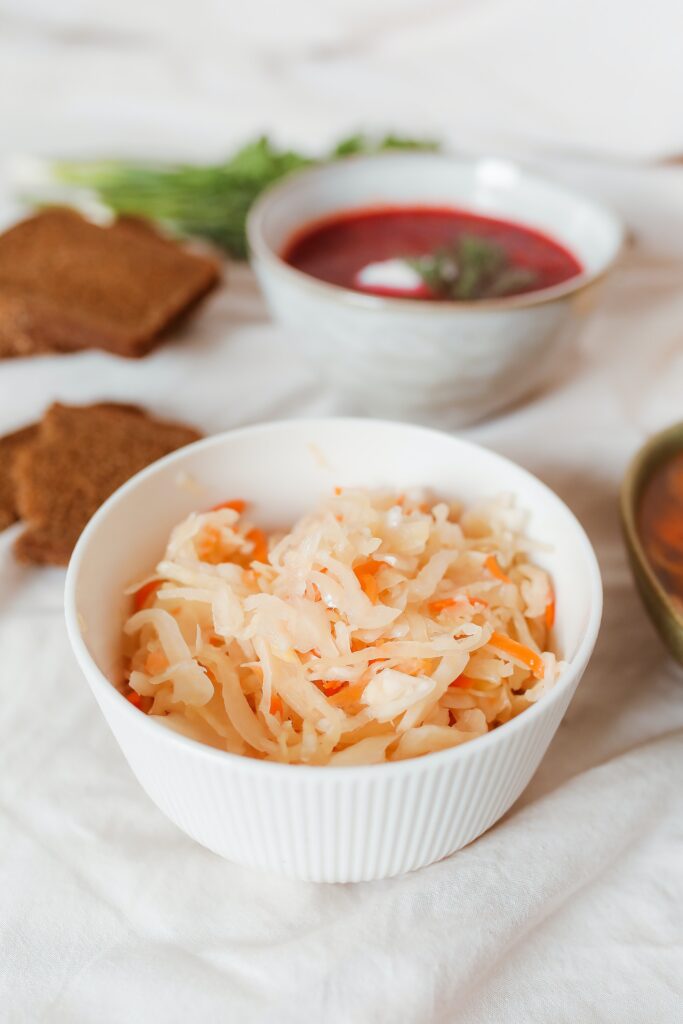 Sauerkraut in a white bowl with rye bread and other side dishes in background.