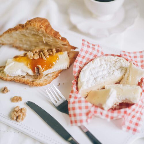 Tangerine jam on a croissant with butter and some nuts. Cup of coffee alongside.