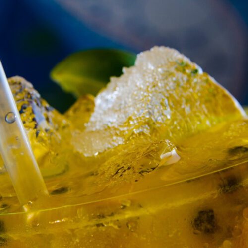 Close-up image of a passionfruit drink with ice and a straw.