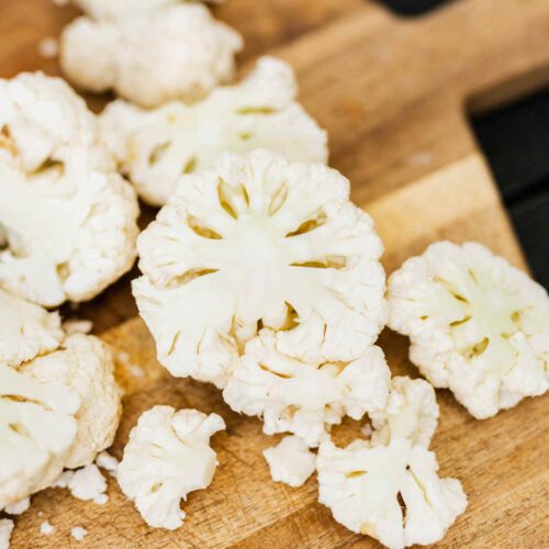 Florets of white cauliflower on a wooden chopping board.