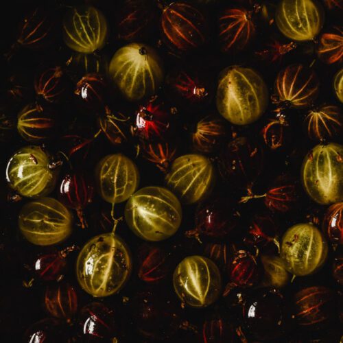 Close up image of red and green gooseberries floating in a syrup