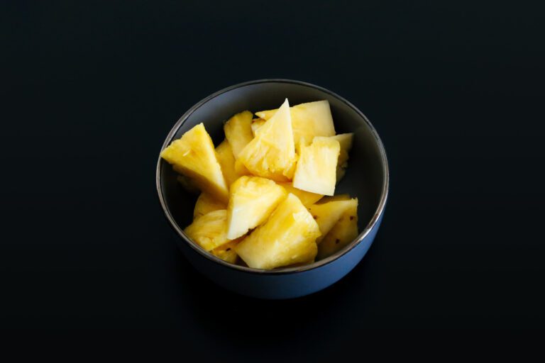 Chunks of pickled pineapple in a black bowl on a dark surface.