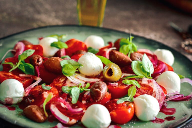 A delicious salad including onion, tomato, olives, balls of mozzarella cheese and basil, drizzled with raspberry vinegar.