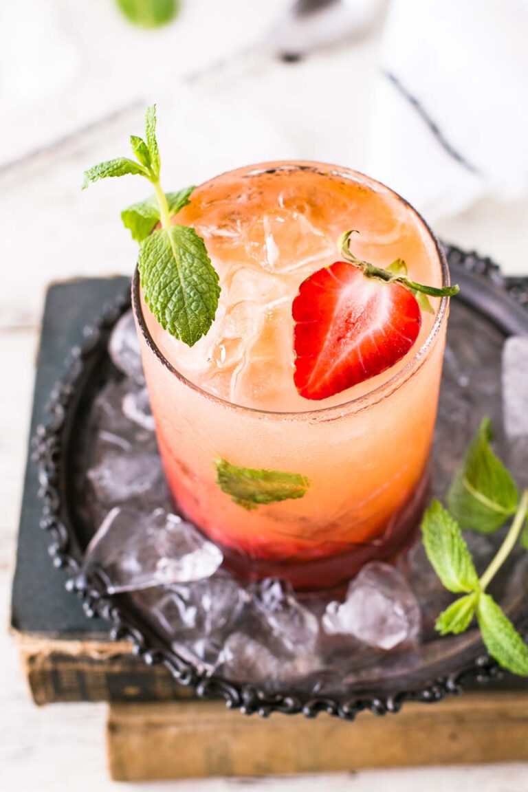 A glass of strawberry mint shrub drink with a sliced strawberry and mint leaf garnish.