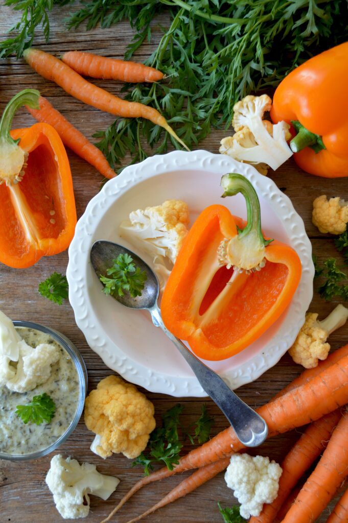 A display of vegetables including cauliflower, sweet peppers (one cut in half) and carrots.