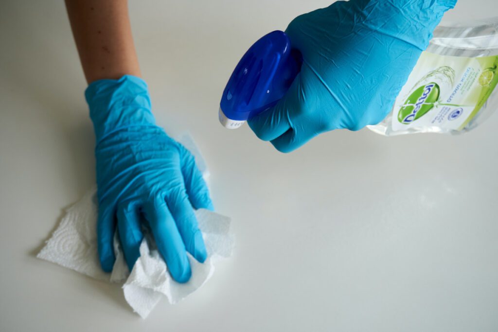 Hands in blue disposable gloves. Cleaning white surface with kitchen towel and antibacterial spray