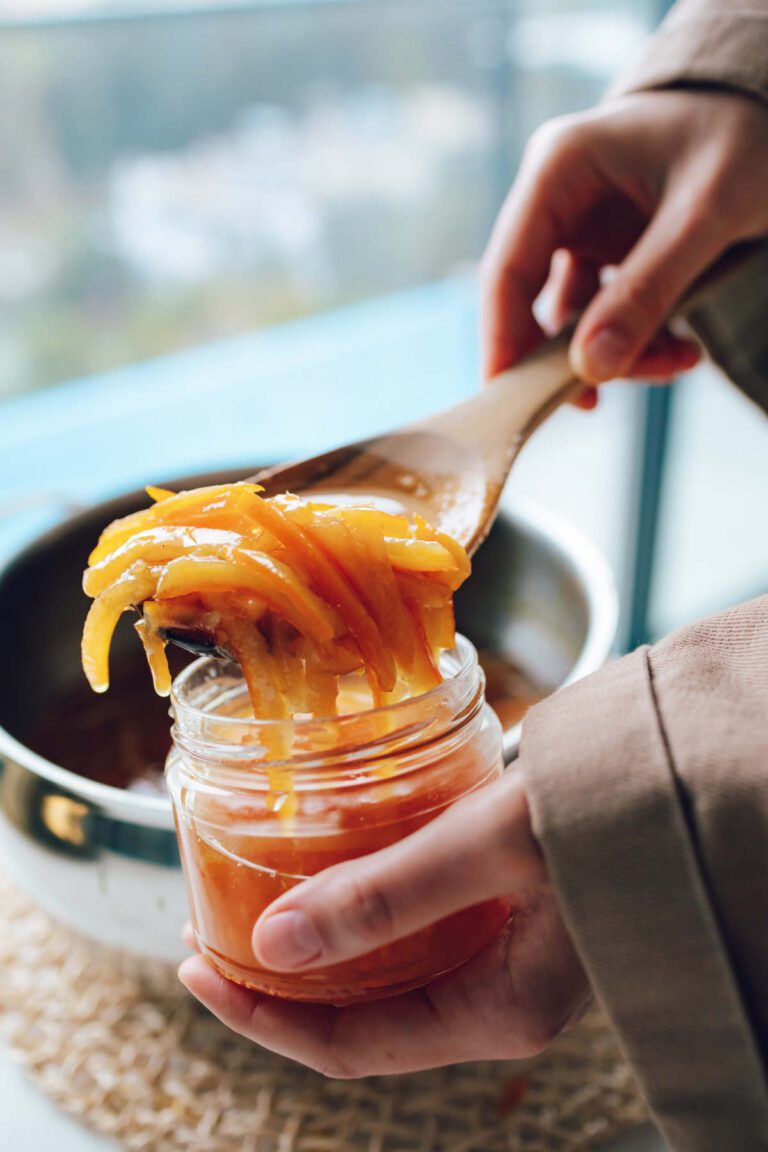 Runny peel heavy marmalade in a wooden spoon being ladled into a glass jar.