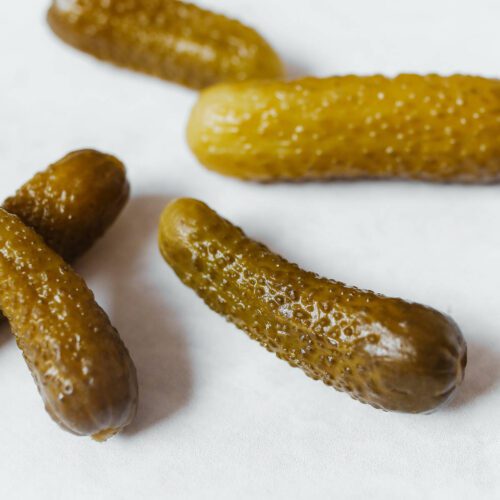 Five whole pickled gherkins on a white surface.